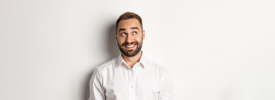 Close-up of handsome man with beard, looking thoughtful at upper left corner, imaging and smiling, white background.