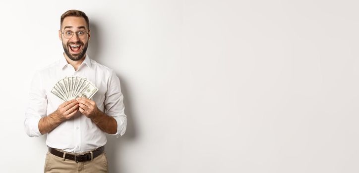 Excited handsome man holding money, rejoicing of winning cash prize, standing over white background.