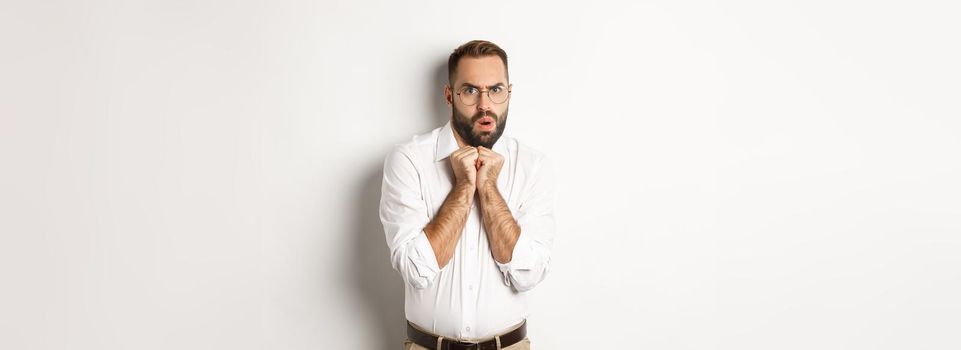 Scared and timid businessman looking anxious, trembling from fear, standing over white background.