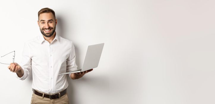 Professional confident businessman doing job on laptop, looking satisfied, standing over white background.