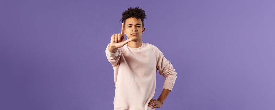 Not so fast, stop. Portrait of young serious-looking hispanic elder brother scolding sibling, forbid coming outside, shaking finger with serious confident face, prohibit action, purple background.