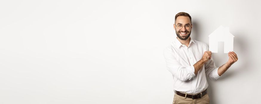 Real estate. Handsome man showing house model and smiling, broker showing apartments, standing over white background.