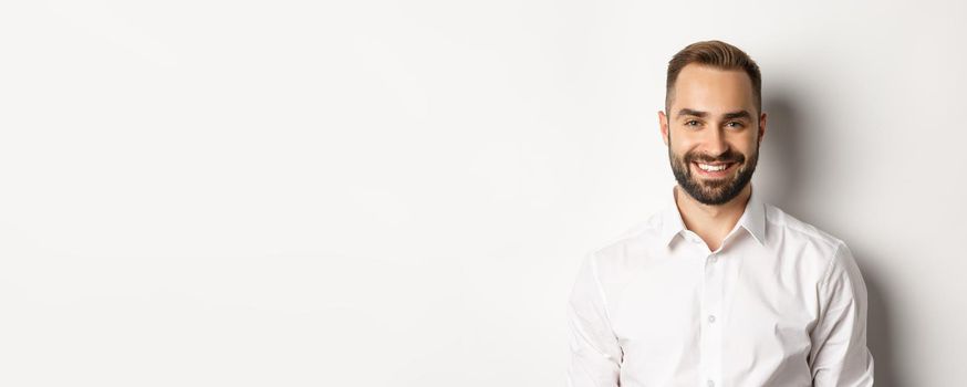 Close-up of confident male employee in white collar shirt smiling at camera, standing self-assured against studio background.