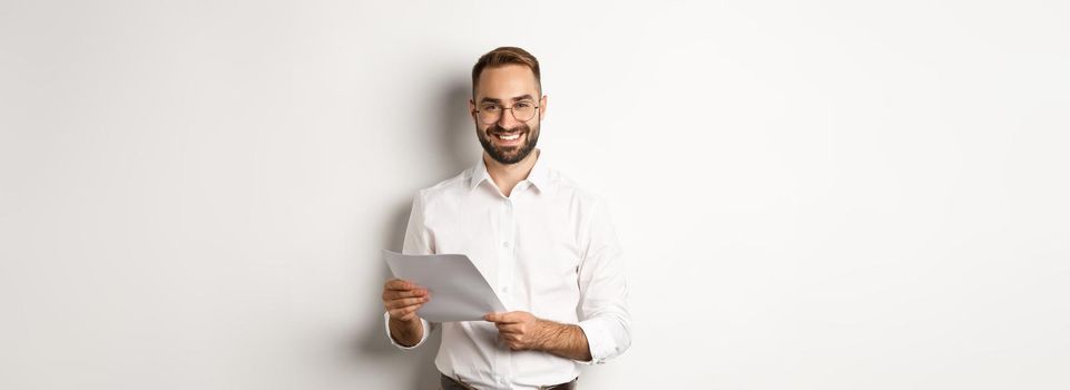 Employer looking satisfied with work, reading documents and smiling pleased, standing over white background.