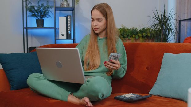 Planning budget. Rich student girl child kid counting money cash use laptop computer calculate domestic bills at home. Young woman satisfied of income earnings, saves money for planned vacation, gifts