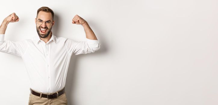 Successful manager flex biceps, showing muscles and looking confident, standing over white background.