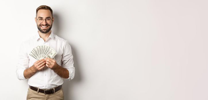 Smiling handsome man holding money, showing dollars, standing over white background. Copy space