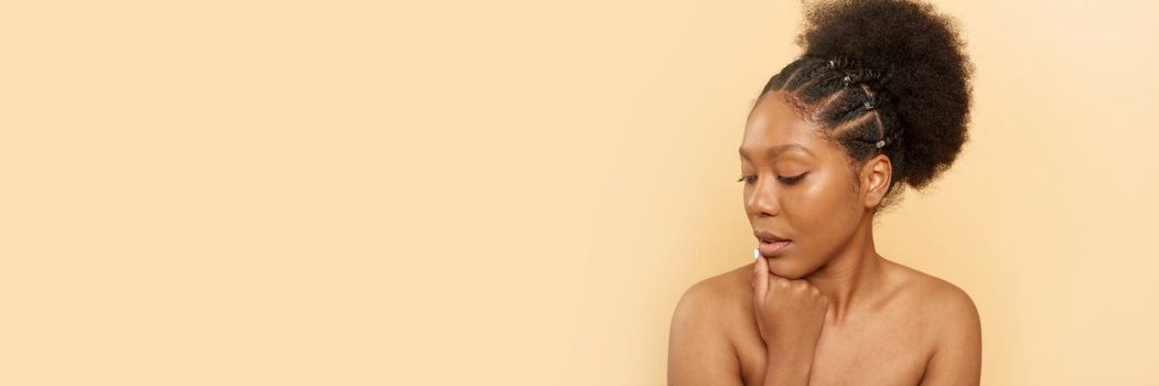 Positive young black woman with bare shoulders and beautiful skin on a beige background. Web banner.