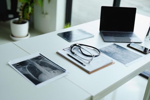 Stethoscope, patient x ray film, important documents and computer on doctor's desk.