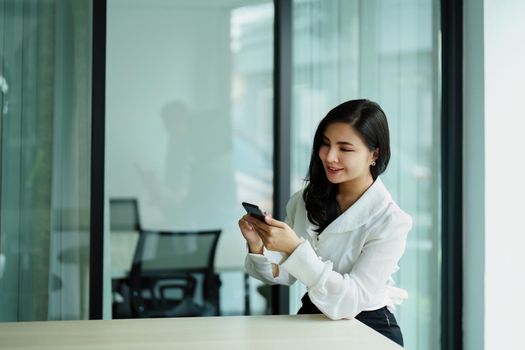 Portrait of a young Asian woman sitting at a desk using her phone.
