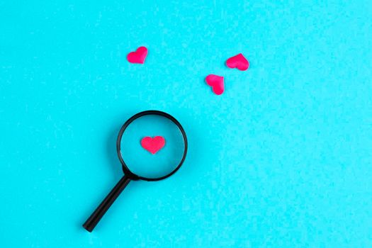 heart lies under a magnifying glass, among many other hearts on a light blue background. The concept of searching for love, find love. Love background. romantic minimalism background.