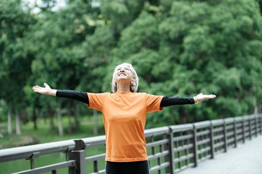 Athletic Senior woman jogger warming up by stretching two arms and upper body before running in park.