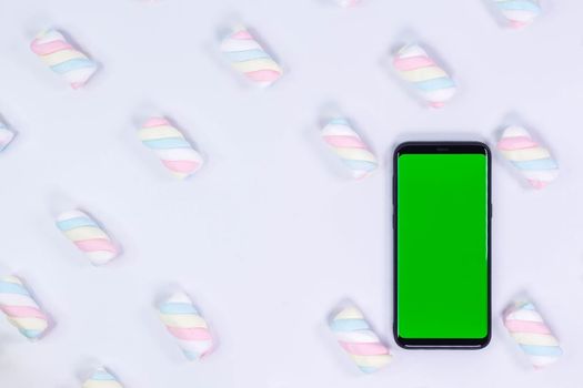 Phone mobile telephone with a vertical green screen. White background with twisted marshmallow pattern. Chroma key smartphone technology.