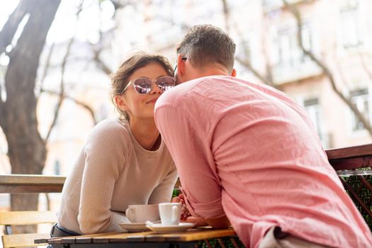 Flirting in a cafe. Beautiful loving couple sitting in a cafe drinking coffee and enjoying in conversation. Love, romance, dating. Man and woman sitting outside cafeteria enjoy coffee