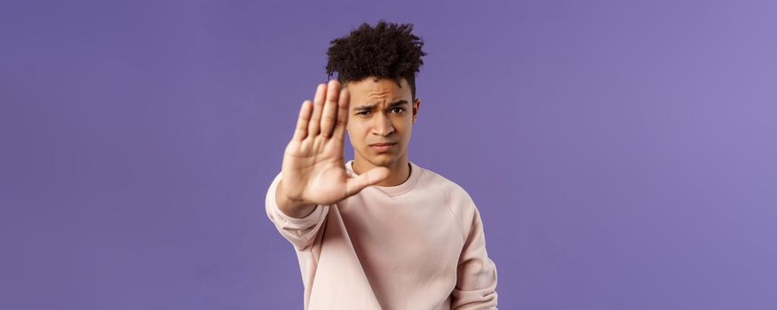 Man you should stop. Close-up portrait of young serious-looking male friend trying to warn person of doing something bad, raise hand to prohibit, forbid no trespassing, purple background.