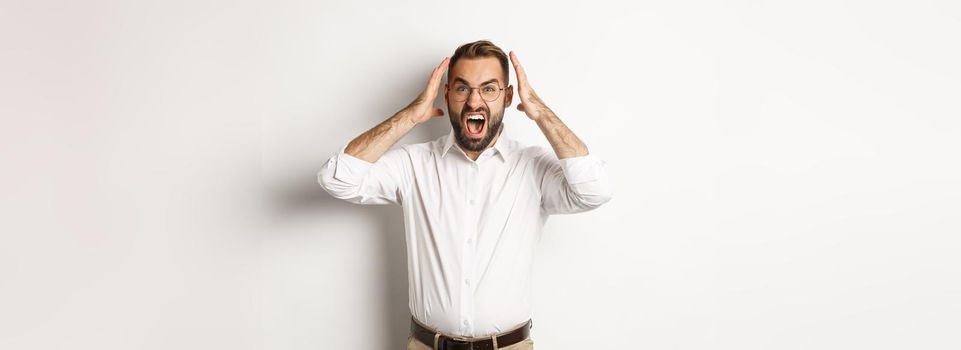 Frustrated man panicking, shouting and looking anxious, standing over white background.