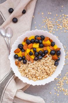 Oatmeal porridge with blueberries, mango and almonds in bowl on concrete grey table from above. flatlay. Healthy breakfast food. Copy space