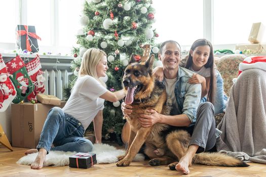 Excited girl and her family sitting on the floor near christmas tree and smiling. family during Christmastime.