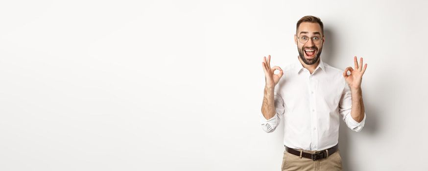 Amazed entrepreneur showing okay sign and looking happy, satisfied with product, standing over white background. Copy space