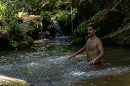 young man in the river in swimsuit splashing water with his hands