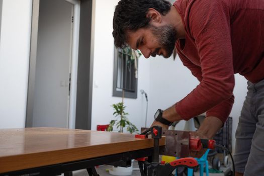 young man using carpenter's power tools making wooden furniture in his home