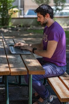 young man working at his computer on a wooden table in the park on a sunny day