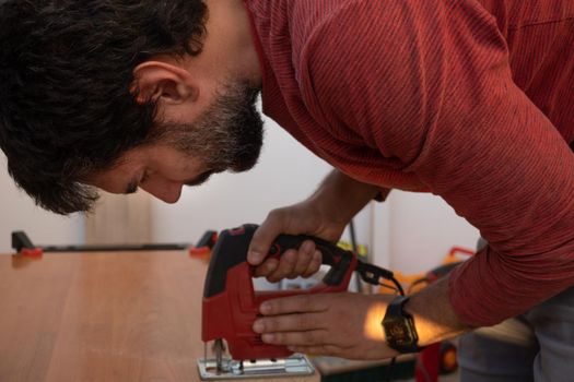 young man using carpenter's power tools making wooden furniture in his home