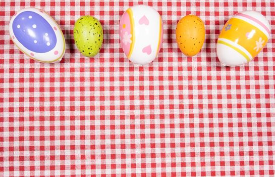Mix of easter eggs of all colors and sizes on a background of red and white gingham fabric. Easter concept.