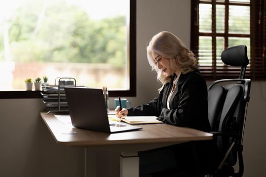 Asian woman writing making list taking notes in notepad working or learning on laptop indoors- educational course or training, seminar, education online concept