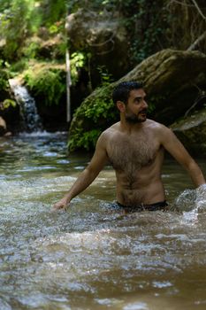 attractive young man bathing in a mountain river with a waterfall in the background