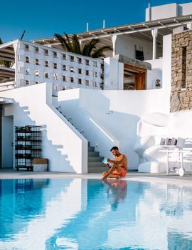 young men in swimming shorts reading a book by the swimming pool. Tanning white men reading a book by the pool