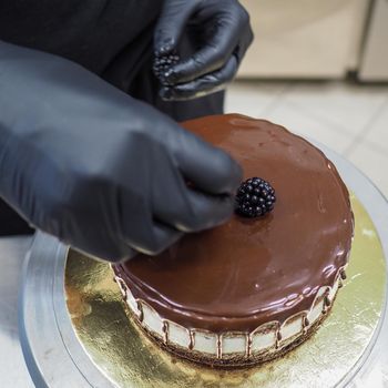 hand of chef toppig a choco cake with gold and berries in the lab