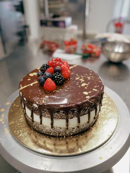 hand of chef toppig a choco cake with gold and berries in the lab