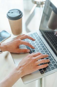 Hands typing on a computer keyboard over a white office table with a cup of coffee and supplies, top view