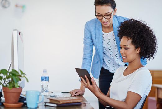 Sharing technology and ideas. two young designers talking together over a digital tablet in an office