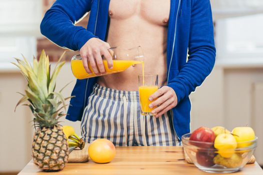 Close up photo Body part young athletic fitness handsome man pours a glass of fresh orange juice in the kitchen at home in casual clothing