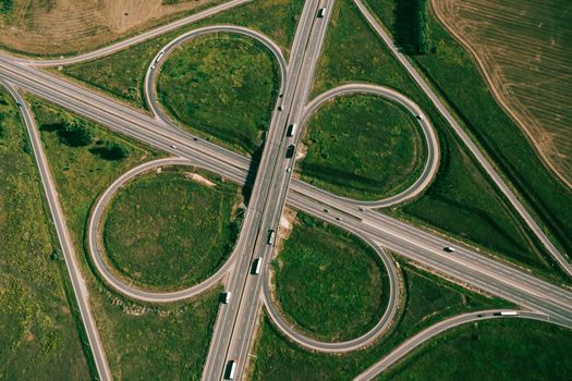 Clover or daisy type of road junction. Aerial top down view of beautiful highway road junction in clover shape at summer day. Lorry truck and semi-truck on highway. Logistic concept