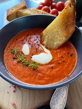 Tomato soup with thyme in a bowl. Dark background. Close up. Top view. Vertical image