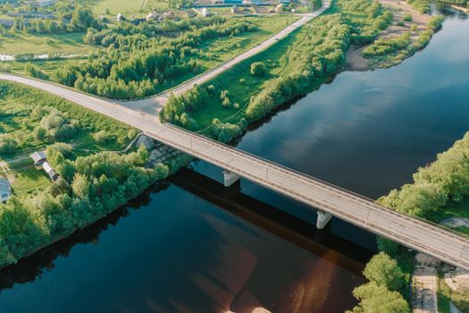 Drone view of empty car bridge crossing beautiful blue river. Aerial perspective view bridge near houses in bright summer. Sunset light. Amazing drone shot