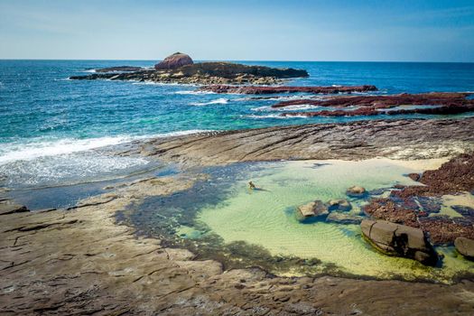 Female in bikini relaxing in a large sandy bottom ocean rockpool with views to other rocks in outer reef. 
 Sapphire Coast of NSW Australia
Travel, recreation,