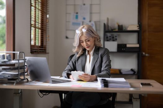 Beautiful asian businesswoman analyzes charts using laptop and calculator. financial accounting, budget and loan paper in office