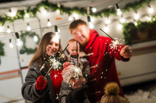 Happy family celebrates christmas in nature and holds sparklers. Parents with three sons travels in a van