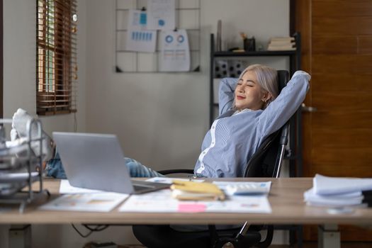 Business asian woman relaxing with hands behind her head and sitting on an office chair.