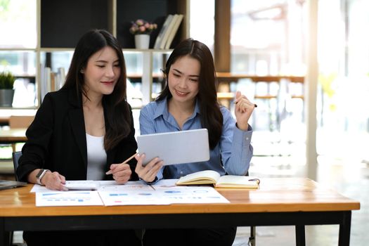 Two young Asian business woman talk, consult, discuss working with new startup project idea presentation analyze plan marketing and investment in the office..