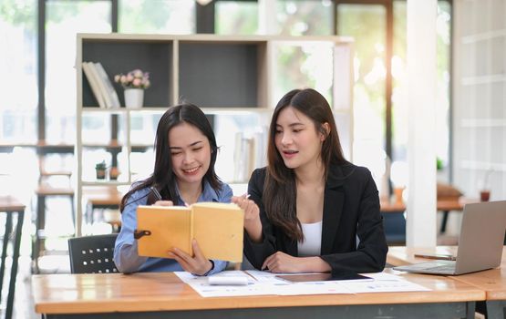 Two young Asian business woman talk, consult, discuss working with new startup project idea presentation analyze plan marketing and investment in the office..