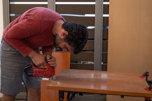 young man using carpenter's power tools making wooden furniture in his home