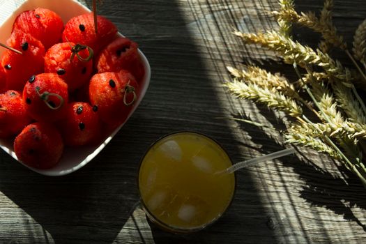 Freshly squeezed orange juice, sweet watermelon dessert and spikelets of ripe wheat on a wooden table in the sunlight...