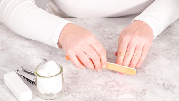 Woman finishing her manicure at home with simple manicure tools. Filing nails with a nail filer.