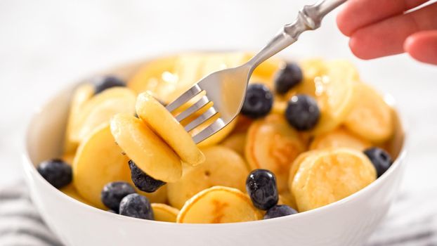 Step by step. Freshly made mini pancake cereal with fresh blueberries in a white bowl.