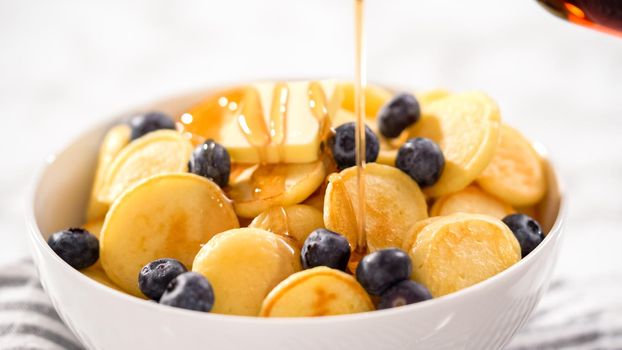 Step by step. Freshly made mini pancake cereal with fresh blueberries in a white bowl.